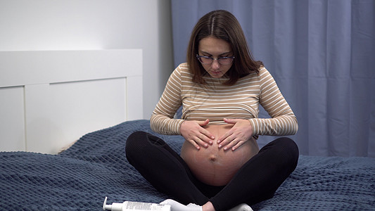 肚子上戴眼镜涂霜的年轻怀孕妇女 床上卧室里的女孩儿们图片