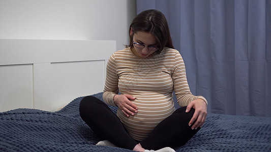 怀着眼镜的年轻孕妇在肚子上打探 卧室里的那个女孩躺在床上 摄像机放大家庭分娩护理保健腹部产妇身体母亲卫生妈妈图片