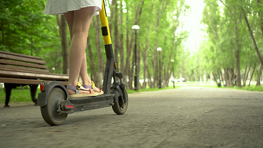 穿着白裙子的年轻女子骑着共用电动摩托 在公园里工具女性自行车城市运输学生街道游客骑术手机图片