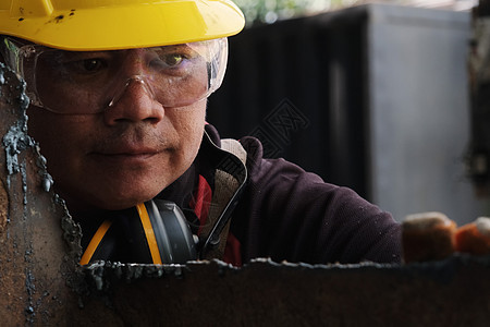 身戴护目镜和建筑手套的男性工人在家庭车间用角研磨机粉碎金属后 对工作进行检查图片