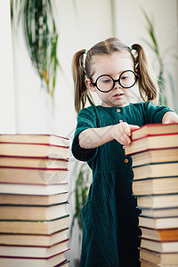 小可爱的学龄前女孩 在书堆之间的圆形玻璃杯上图片