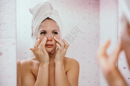 年轻漂亮的女人在洗完澡后使用保湿面膜 头戴毛巾的漂亮迷人女孩站在家庭浴室的镜子前 日常卫生和皮肤护理胶原产品调色洗涤粉刺享受预防图片