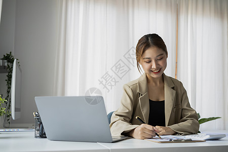 美丽的女雇员使用笔记本电脑 在笔记本上做重要笔记图片
