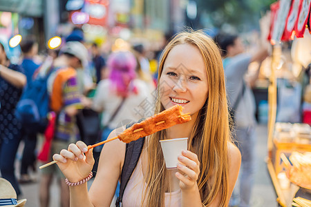 在首尔的一条步行街道上吃典型韩国街头食物的年轻女游客 在南韩当地马特克Soul Korea只发现一些辣妹快餐市场美食街道小贩油炸图片