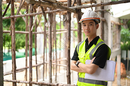 戴头盔和安全反光背心的迷人男性检查员 主管或建筑建筑师在建筑工地交叉双臂站立图片