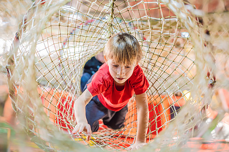 男孩在障碍课程中爬到网上训练安全平衡男生活动挑战培训绳索电缆冒险图片