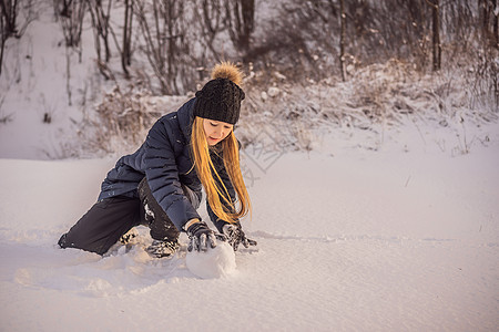 年轻女子滚滚巨型雪球来造雪人男人滚动乐趣女孩降雪运动暴风雪女士手套寒冷图片