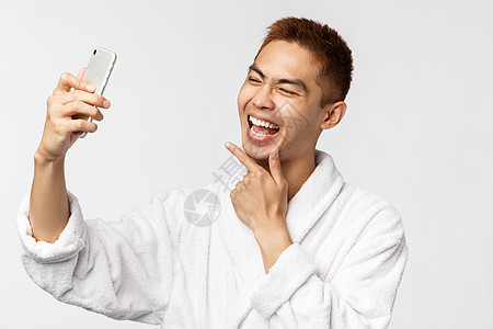 美人 SPA和技术概念 浴袍中快乐的亚洲男子肖像在家中花费了19年的社会舞蹈隔离 取自拍 看手机相机时很可爱图片