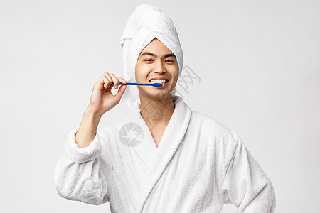 美容 水疗和休闲概念 穿着浴袍和浴巾的乐观快乐的亚洲男人 用牙刷刷牙 微笑 注意个人卫生 白色背景图片