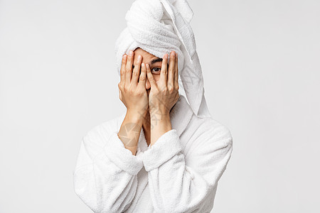 穿着浴袍和头顶浴巾的有趣的亚裔男子 从淋浴中出来 躲在手后面 用一只好奇的眼睛 白色背景偷看 (笑声)图片