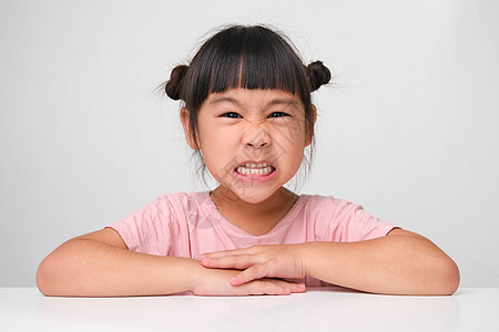 坐在一张白色背景的桌子上 看着摄像机 脸色发热的可爱黑头发小女孩 笑声学校幼儿园孩子学生教育侵略女儿压力童年情感图片