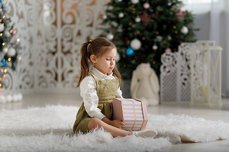 在圣诞节内地坐在地毯上时 带着新年礼物的心烦的小姑娘图片