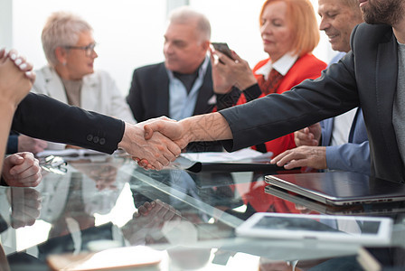 商界人士在现代办公室与同事齐聚一桌的同僚握手图片