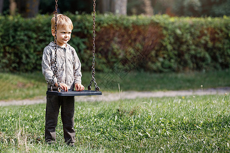 一个有吸引力的小男孩站在市公园里 带着铁链的摇摆旁 一个孩子准备挥舞 横向照片童年阳光休闲男性金发假期享受晴天院子游戏图片