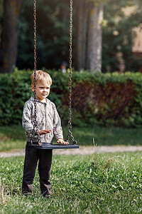 一个有吸引力的小男孩站在市中心公园 带着铁链的摇摆旁 一个孩子准备挥舞 垂直照片男性闲暇乐趣金发晴天快乐喜悦游戏院子活动图片