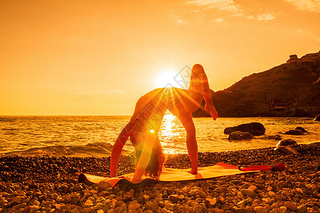 中年漂亮的女人 一头黑发 在卵石滩海边的瑜伽垫上用戒指做普拉提 女性健身瑜伽概念 健康的生活方式 和谐与冥想讲师活力运动员活动绑图片