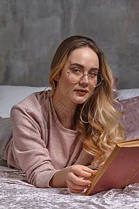 戴眼镜的金发女士 穿着休闲服 她正看着你 拿着书 躺在卧室的床上 学生 博主 文档研究 特写图片