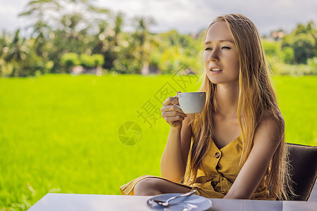 Corona病毒已经结束 检疫措施被削弱 摘下面具 现在你可以到公共场所去 在印度尼西亚巴厘的稻田露台附近的咖啡厅阳台上喝茶的女图片