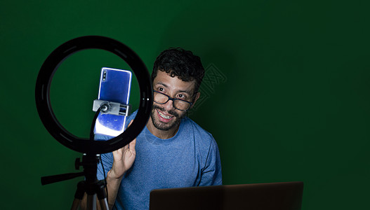 带笔记本电脑制作视频博客的年轻人 带手机的年轻人内容创作者 带笔记本电脑制作绿色背景视频通话的男人面试职场工作室创造者灯光博主摄图片