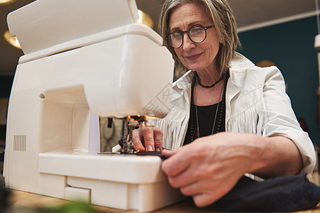 一位时装设计师裁缝在裁缝工作室的制造缝纫机上缝制黑布 时尚设计理念图片