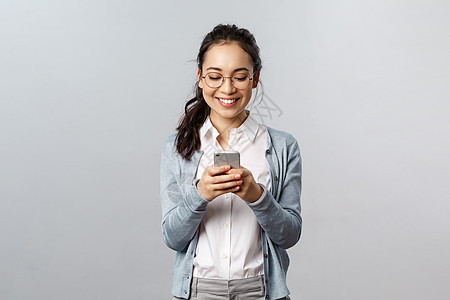 办公室生活方式 商业和人的概念 快乐开朗的韩国女性给朋友发短信 使用手机 对着智能手机显示屏微笑 进行有趣的交谈 在线观看视频享图片