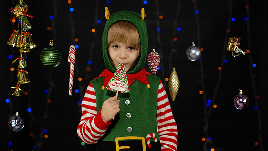 小女孩穿着圣诞精灵圣诞老人助手服装舔着糖果棒棒糖焦糖糖果图片