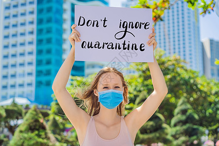戴医用面具的妇女可以预防冠状病毒病 她举着一张海报 不要忽视检疫的手写文字-用白色隔离的字母 冠状病毒 COVID 19 概念图片