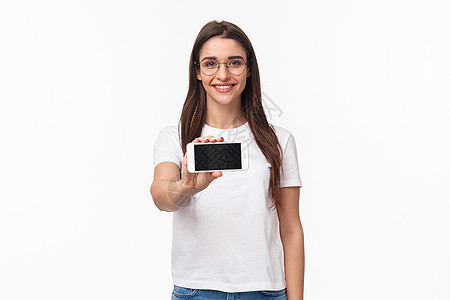 通信 技术和生活方式概念 戴眼镜和 T 恤的年轻迷人女性肖像 水平显示智能手机屏幕 介绍游戏或应用程序乐趣微笑快乐折扣假期商业工图片