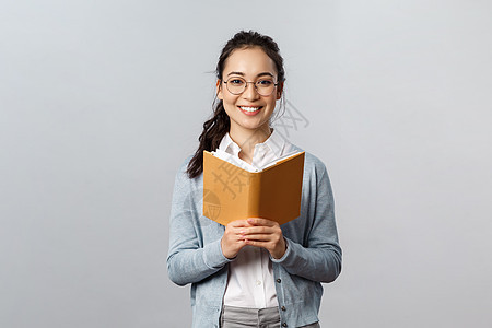 教育 教师 大学和学校的概念 年轻聪明而有创造力的亚洲女学生读她的家庭作业或诗歌 学习考试 拿着计划书或笔记本 微笑的相机女孩工背景图片