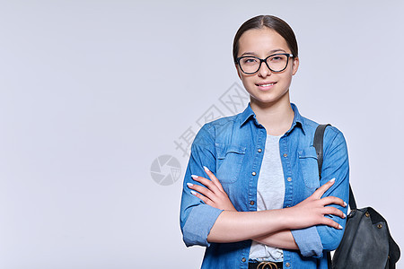 戴眼镜 背着背包的年轻女学生在光背景下观看相机学校女孩蓝色学习班级学费青春期青少年工作室牛仔布图片