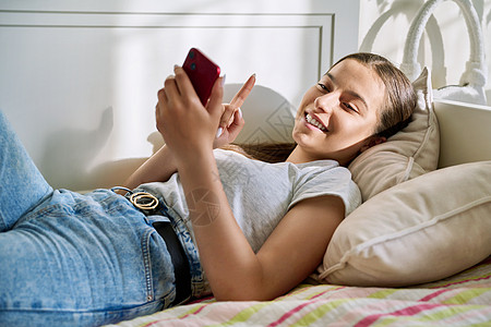 少年少女美丽的年轻少女用智能手机躺在沙发上休息的睡椅上青少年娱乐故事视频游戏闲暇互联网技术社交喜悦背景