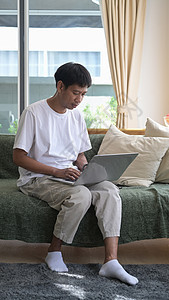 坐在明亮起居室时使用电脑笔记本电脑的青年男子全镜头图片