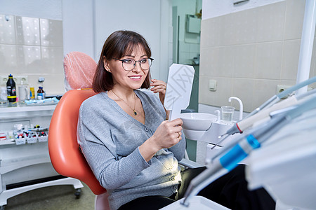 微笑的中年妇女坐在牙椅上 用镜子照着她的牙齿图片