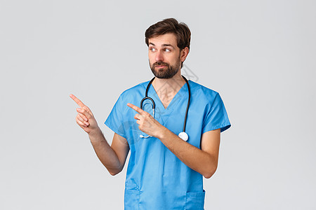 医护人员 流行病和冠状病毒爆发的概念 不确定和优柔寡断的大胡子医生 医生或护士在磨砂 听诊器 假笑 指着左好奇图片