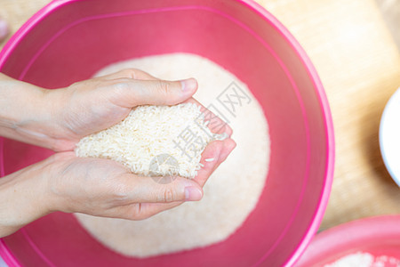 顶视图女人手拿着红色塑料碗上方的米饭 全球粮食危机 生干米饭 未煮过的精白米饭 Zakat 和慈善理念 有机谷物 世界市场上的大背景图片