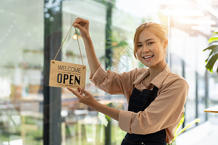 商店店主通过门玻璃把开关的标志打开 准备服务 Asian女性小型商业概念快乐图片