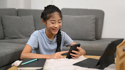 性格开朗的亚洲女孩在网上学习休息时使用智能手机 电子学习 家庭教育概念图片