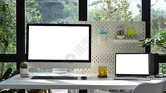 现代工作场所白色桌子上的混合计算机 膝上型电脑 笔记本电脑 房屋种植和用品 广告屏幕空白图片
