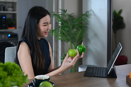 快乐的年轻女子在厨房准备蔬菜沙拉时 阅读数码平板电脑配方图片