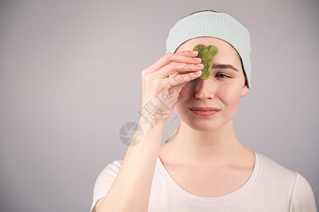 一个年轻女人的肖像 用白色背景的狗脸刮刀 按摩她的脸化妆品刺激女性皮肤调色温泉宝石治疗剥皮享受图片