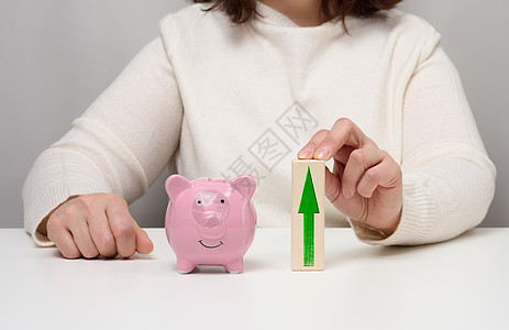 粉红陶瓷小猪银行和用箭头的木块 在银行存款中利息增加的概念图片