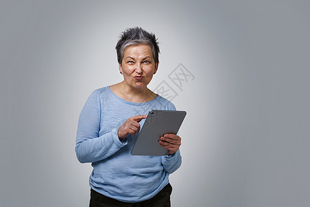 拥有数字平板电脑工作或检查社交媒体的白发成年妇女 50多岁穿蓝衬衫的美貌女性在白色背景上与白人隔绝了50多岁图片