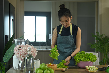年轻女子站在厨房桌前 准备制作新鲜蔬菜沙拉的原料和素材 (笑声)图片