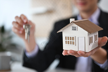 年轻的房地产经纪人拿着房子模型和钥匙 房地产投资和保险概念图片