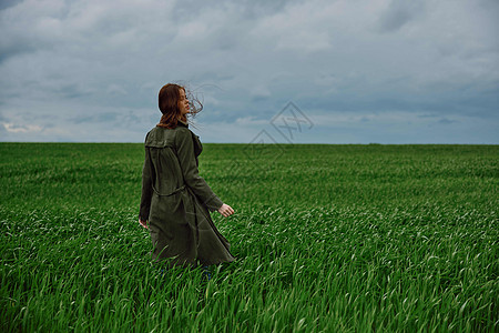 一个穿着长长雨衣的女人 站在风暴的绿地上 背对着镜头土地国家地平线爬坡场地天空女性外套小麦成人图片