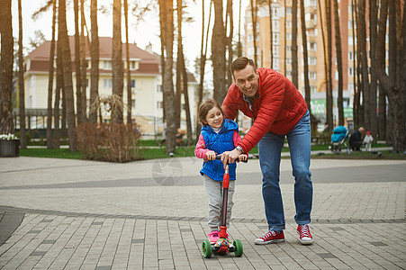 一个迷人的慈爱父亲和他 5 岁的女儿在森林公园户外骑滑板车的幸福友好家庭 积极的生活方式 为人父母 童年图片