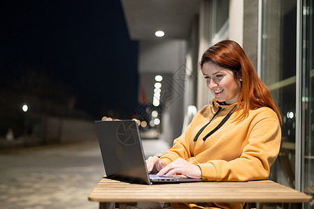 深夜 一位女士在夏季咖啡馆的笔记本电脑前远程工作 一个微笑的女孩坐在一张废弃的街道上的一张木桌旁学习商业咖啡店电子商务考试教育潮图片