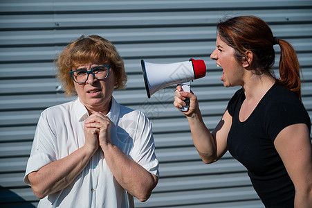 世代冲突 一位愤怒的中年妇女通过扩音器对一位年迈的母亲大喊大叫 一个成年女儿通过扩音器对一个不开心的养老金领取者尖叫 家庭中的争图片