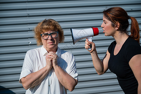 世代冲突 一位愤怒的中年妇女通过扩音器对一位年迈的母亲大喊大叫 一个成年女儿通过扩音器对一个不开心的养老金领取者尖叫 家庭中的争图片