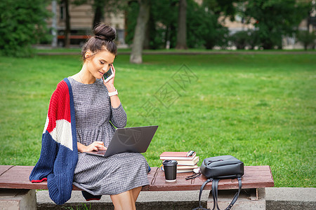 学生在长椅上用智能手机说话微笑闲暇公园女性笔记本学习互联网服装成人技术图片